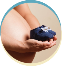 Pregnant woman holding small baby shoes.