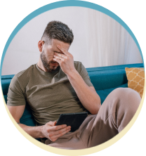 Man with headache looking at tablet on couch.