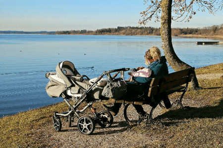 Woman resting with stroller by tranquil lakeside.